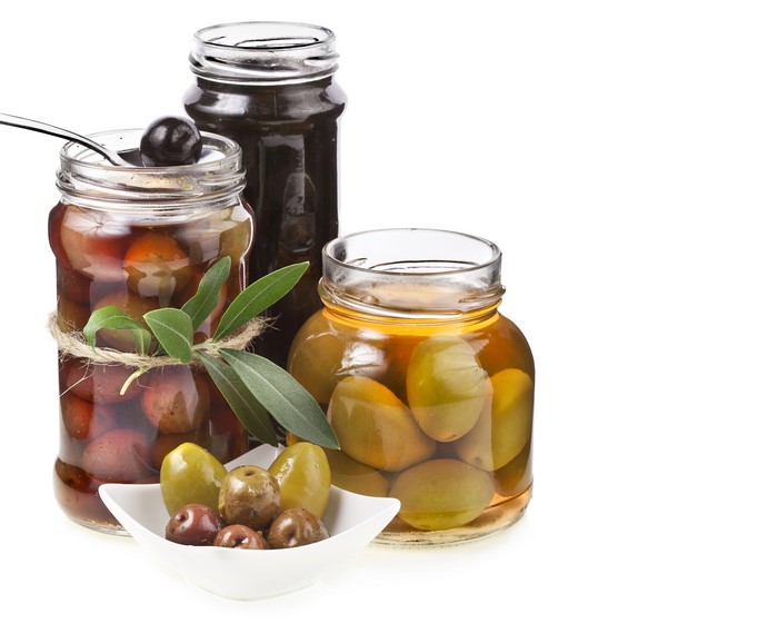 Three jars of olives with a small bowl of olives