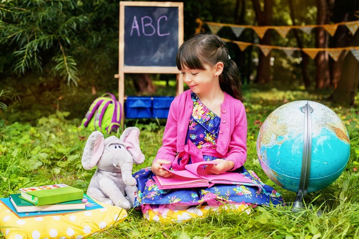 Girl with Elephant Toy, Globe, and Books Outdoors