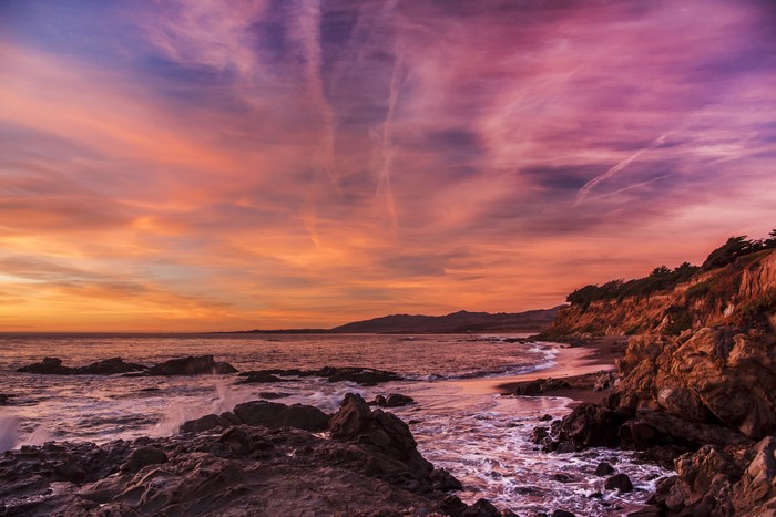Sunset over rocky coast with waves and colorful sky