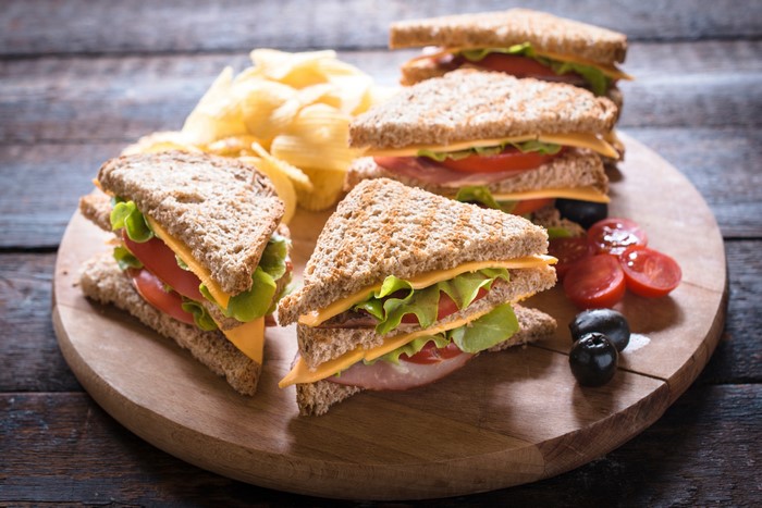 Sandwiches with chips, olives, and tomatoes on a cutting board