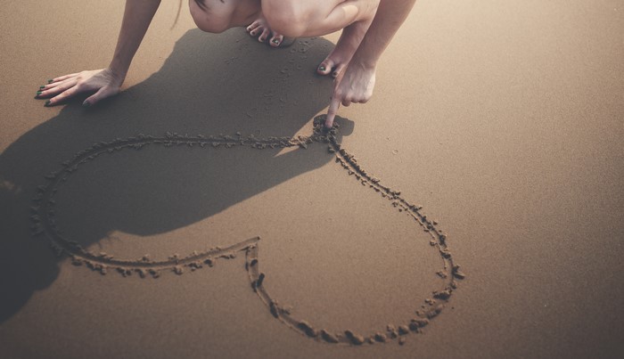 Person drawing a heart in the sand