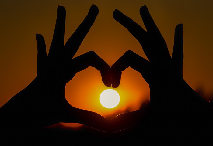 Silhouette of hands forming a heart around the sun at sunset