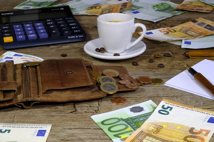 Euro banknotes, coins, calculator, wallet, coffee cup, and pen