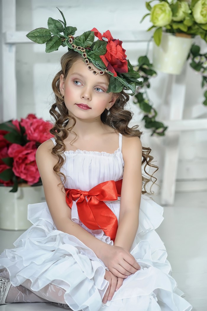Girl in a white dress with a red bow and floral hat