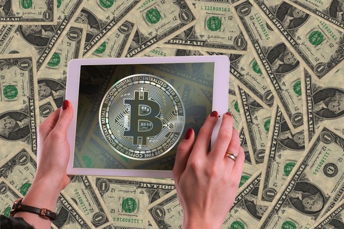 Hands holding tablet with Bitcoin logo over dollar bills