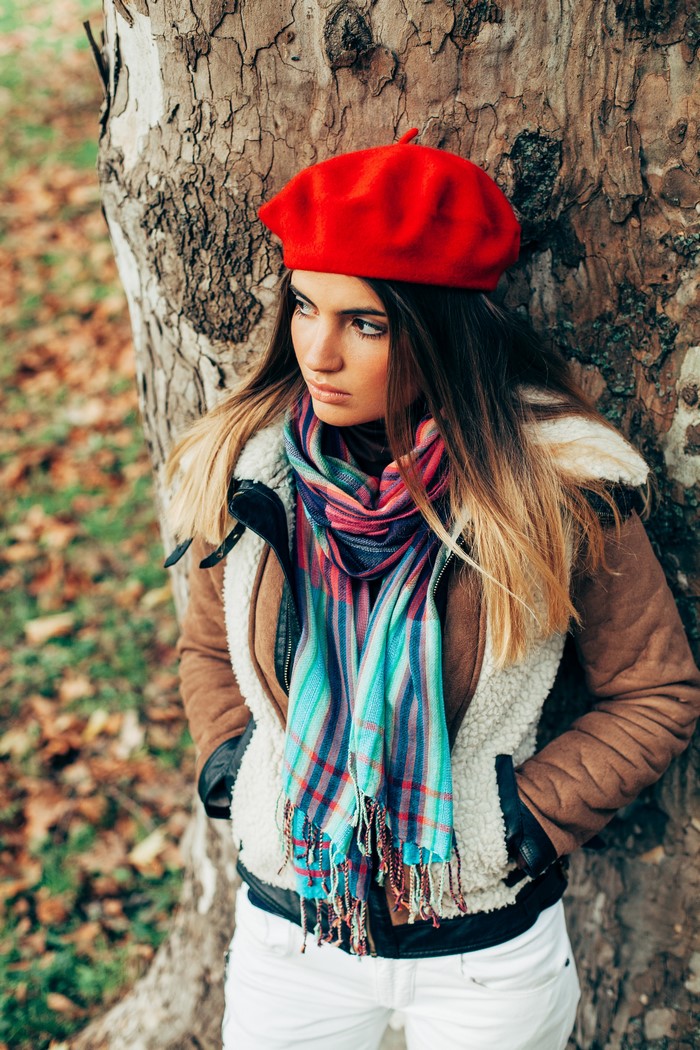 Woman in red beret and scarf leaning against tree