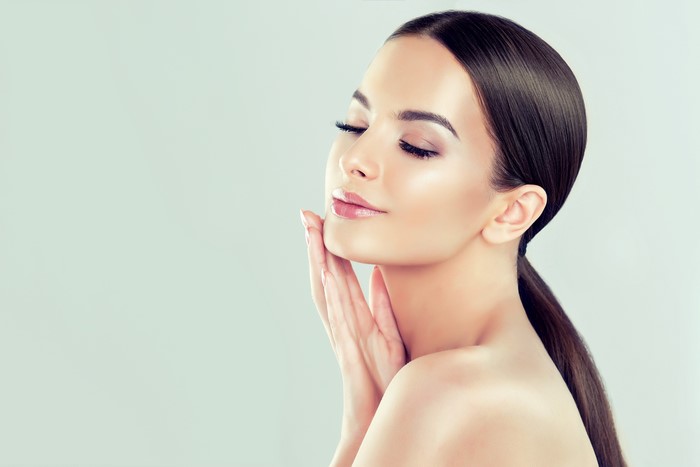 Woman with brown hair and makeup touching her face