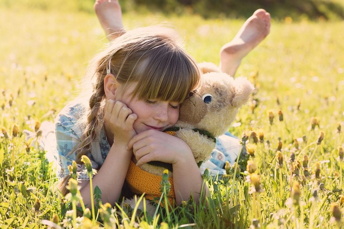 Girl hugging a teddy bear in a grassy field