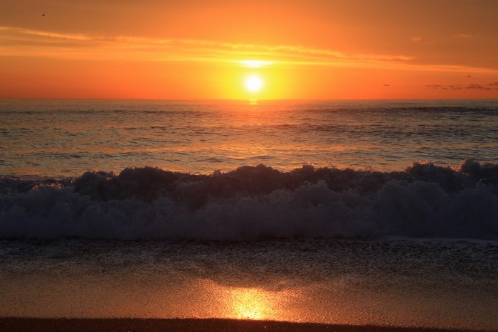 Sunset over the ocean with waves crashing on the beach
