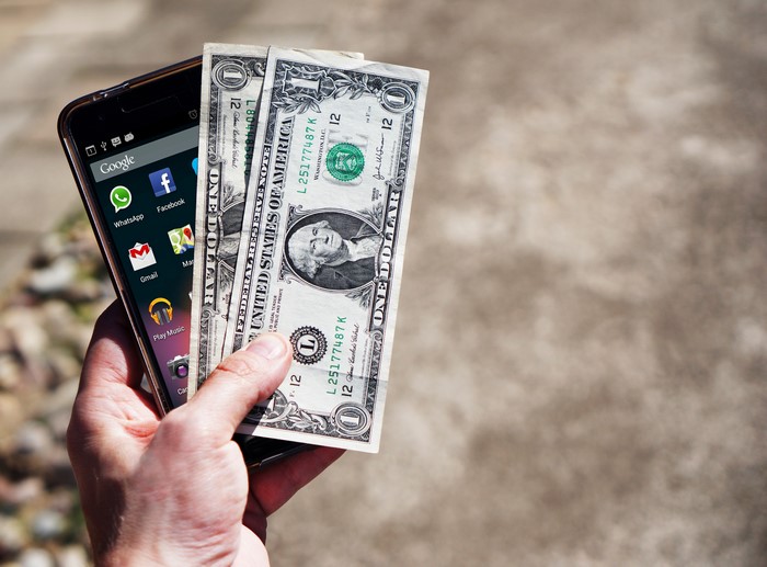 Hand holding smartphone with US dollar bills