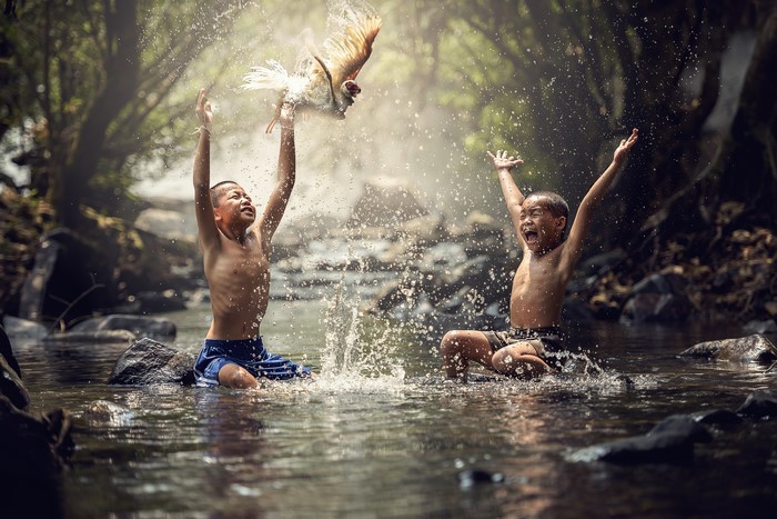 Two Asian boys playing with a chicken in water