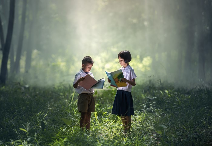 Two Asian children reading books in a forest