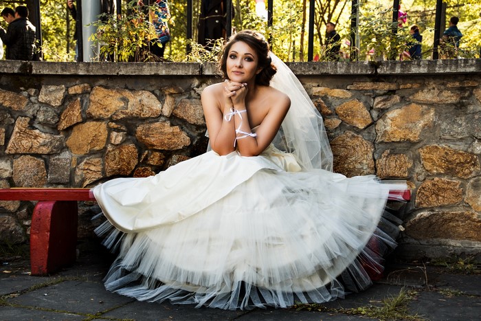 Bride sitting on a bench in front of a stone wall