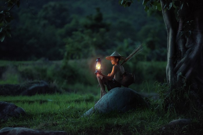 Boy with lantern sitting on a rock in the evening
