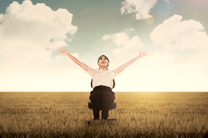 Woman sitting in a field with arms raised