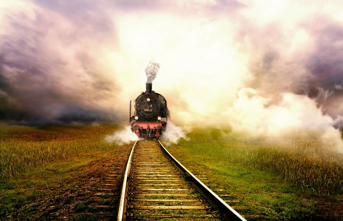 Steam train on railroad tracks through a grassy field