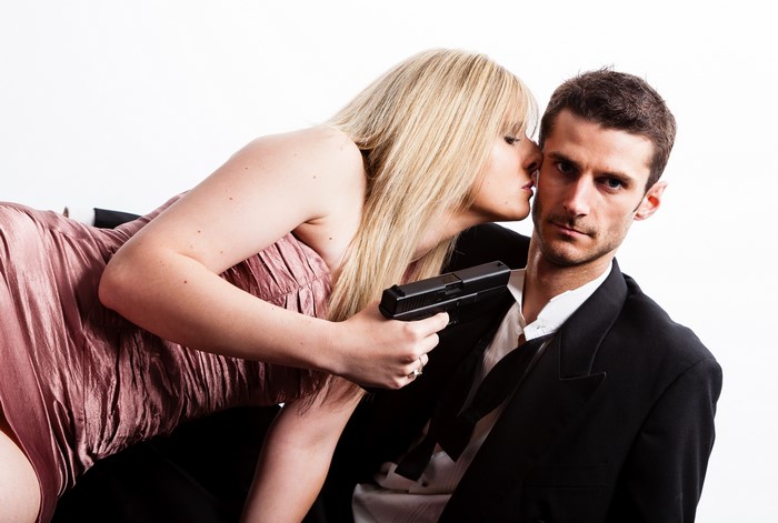 Blonde woman kissing man holding pistol