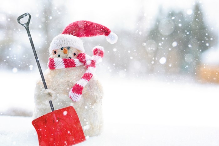 Snowman with shovel and red hat in snow