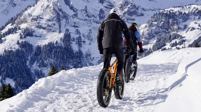 Two people on fat-tire bikes on a snowy mountain trail