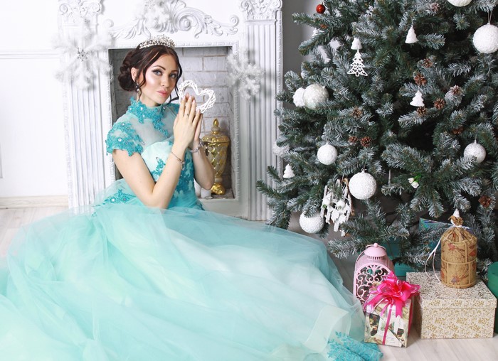 Woman in a blue dress with a tiara by a Christmas tree