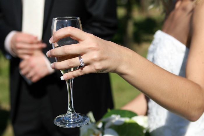 Bride holding champagne glass with groom in background
