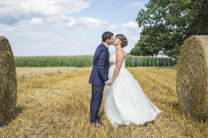 Bride and Groom kissing in a field with hay bales