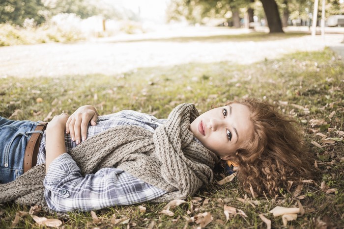 Brown-haired woman wearing a scarf lying on grass