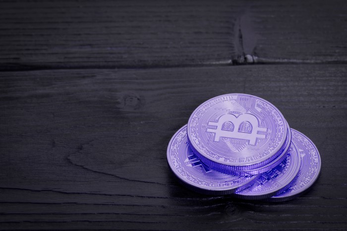 Violet Bitcoin coins on a dark wooden surface