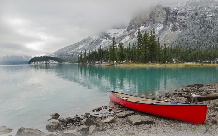 Red canoe on a rocky shore of a turquoise lake with snow-capped mountains