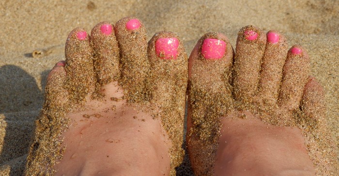 Feet covered in sand with pink toenails