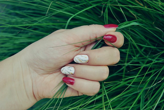 Hand with red and marble nails in grass