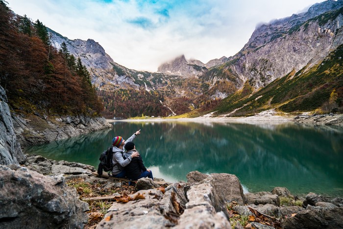 Two people sitting by a lake with mountains