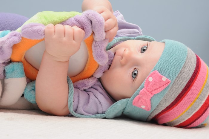 Infant playing with a colorful toy, wearing a striped winter hat