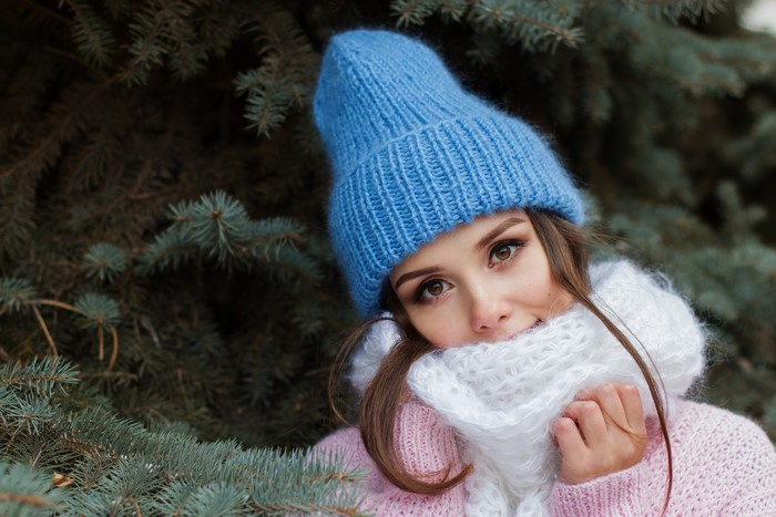 Woman in blue winter hat and white scarf near fir branches