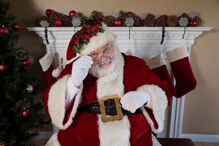 Santa Claus adjusting his glasses by a Christmas tree