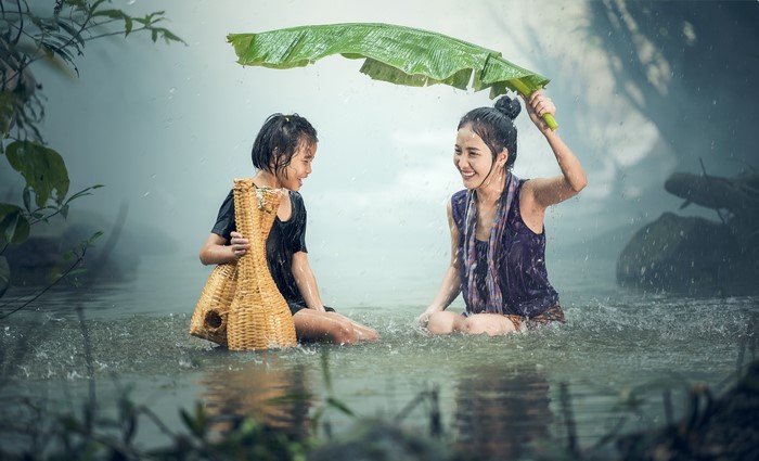 Two Little Girls Laughing and Sitting in Rain with Banana Leaf