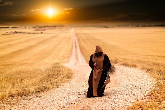 Pilgrim walking on a dirt road through fields at sunset