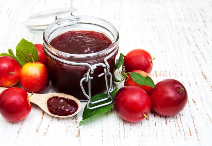 Plum jam in a jar with fresh plums and a wooden spoon