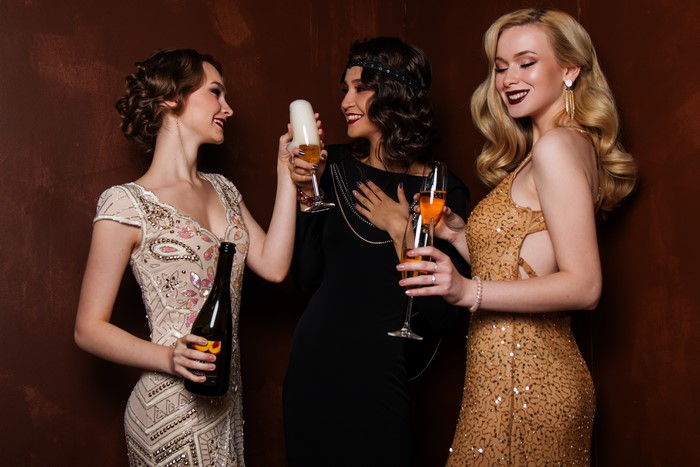 Three women in vintage dresses with champagne