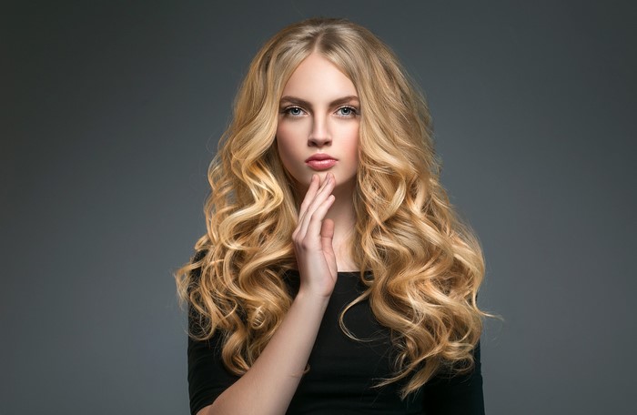 Blonde woman with curly hair on gray background