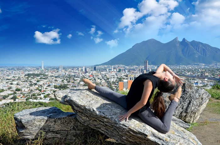 Woman doing yoga on rocks with city and mountains background