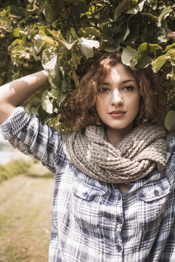 Woman with curly brown hair wearing a scarf and plaid shirt