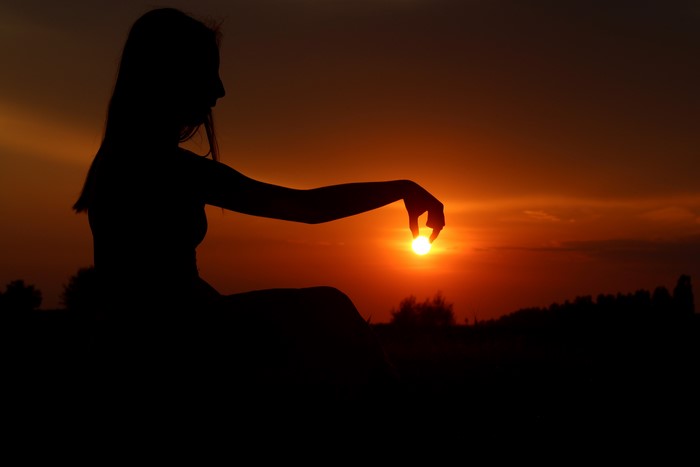 Silhouette of a person holding the sun at sunset