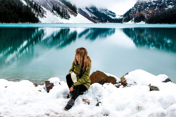 Woman sitting by a snowy lake with mountains