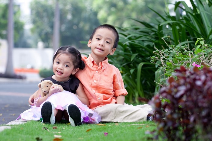 Two Asian children sitting on grass with teddy bear