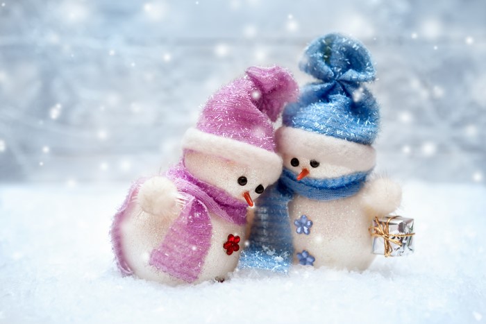 Two snowmen in winter hats and scarves with a gift