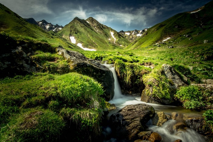 Mountain stream flowing through green hills with snow patches