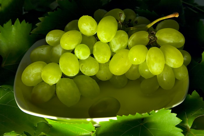 Green grapes on a white plate with leaves