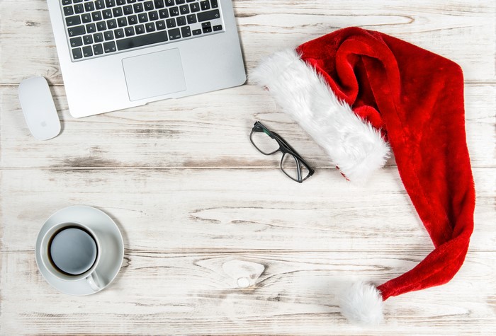 Christmas Santa hat on a wooden desk with laptop, mouse, coffee, and glasses