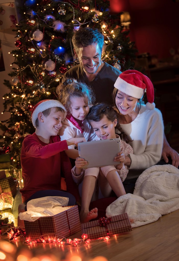 Family with children looking at a tablet by Christmas tree